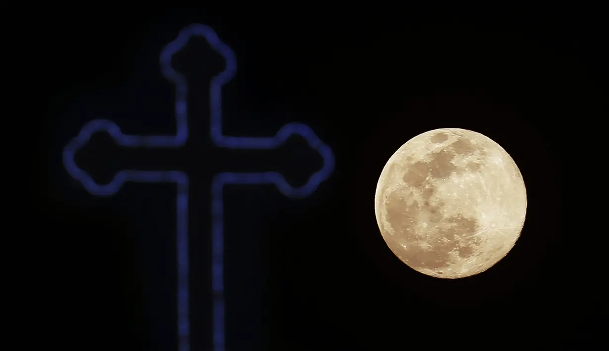 Supermoon terlihat di belakang salib dari gereja Ortodoks Kristen di pinggiran Lakatamia, Nicosia, Siprus, Selasa (7/4/2020). Fenomena dimana bulan berada pada titik terdekat dengan bumi ini merupakan penampakan supermoon terbesar di tahun 2020. (AP Photo/Petros Karadjias)