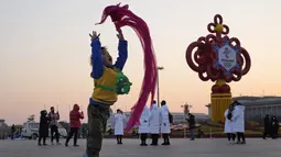 Seorang anak bermain dengan syal merah di dekat dekorasi untuk Olimpiade Musim Dingin Beijing di Lapangan Tiananmen di Beijing, China (18/1/2022). China telah mengunci sebagian distrik Haidian Beijing menyusul deteksi tiga kasus. (AP Photo/Ng Han Guan)