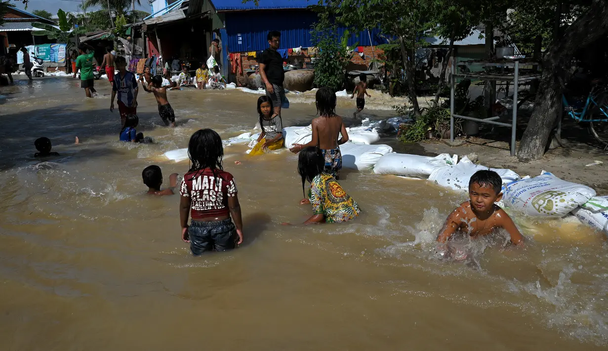 Anak-anak bermain di air banjir setelah hujan lebat di pinggiran Phnom Penh, Kamboja (26/10/2021). Kementerian Sumber Daya Air dan Meteorologi telah mengeluarkan pemberitahuan pada hari Senin tentang situasi cuaca, mengkonfirmasikan risiko banjir di 14 ibu kota dan provinsi Kamboja. (AFP Photo)