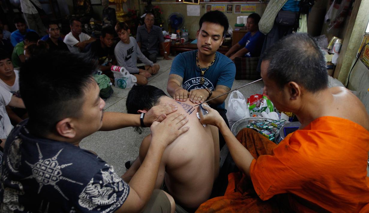 Sejumlah orang menyaksikan seorang pria yang di tato menggunakan jarum tradisional di Wat Bang Phra, Nakhon Pathom, Thailand , (18/3). Orang-orang rela antri untuk mendapat tato dari guru pembuat tato atau Biksu tersebut. (REUTERS / Chaiwat Subprasom)