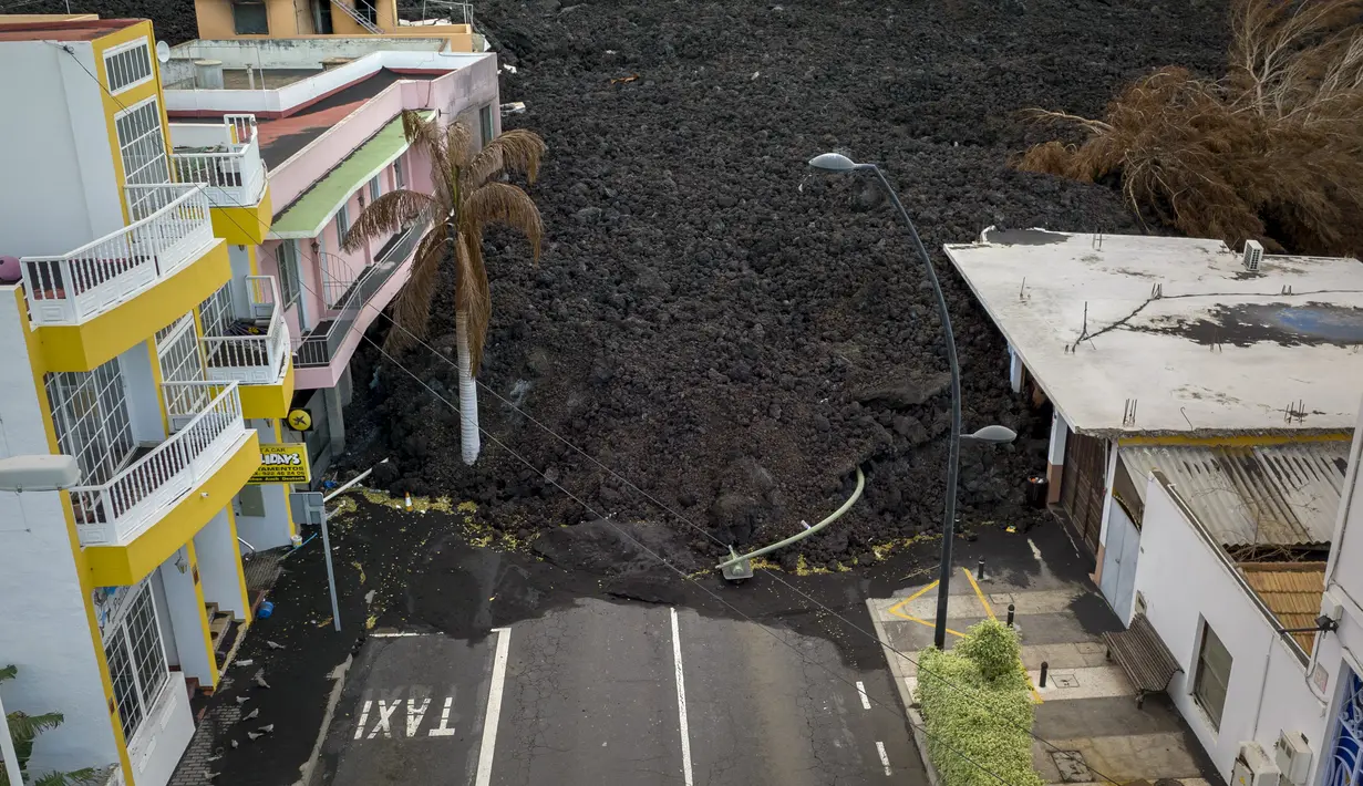 Aliran lahar menghancurkan rumah-rumah saat gunung berapi terus meletus di pulau Canary La Palma, Spanyol, Senin (29/11/2021). Punggung bukit dan mengancam akan memperluas dampak pada tanah yang dievakuasi, infrastruktur dan rumah. (AP/Emilio Morenatti)