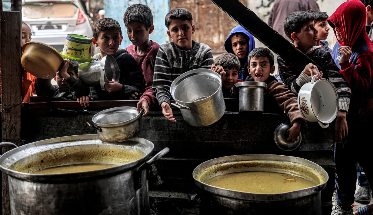 Anak-anak menunggu sambil memegang panci kosong bersama pengungsi Palestina lainnya untuk mendapatkan makanan menjelang berbuka puasa selama bulan suci Ramadhan, di Rafah di Jalur Gaza Selatan pada 16 Maret 2024. (SAID KHATIB/AFP)