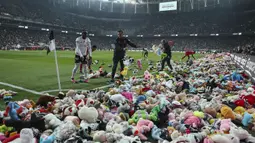 Pemain Besiktas dan Antalyaspor dibantu petugas mengumpulkan boneka yang dilemparkan oleh penonton pada laga lanjutan Liga Turki 2022/2023 yang berlangsung di Stadion Vodafone, Istanbul, Minggu (27/02/2023). Aksi tersebut ditujukan sebagai bentuk sumbangan untuk anak-anak korban gempa Turki. (AP Photo)