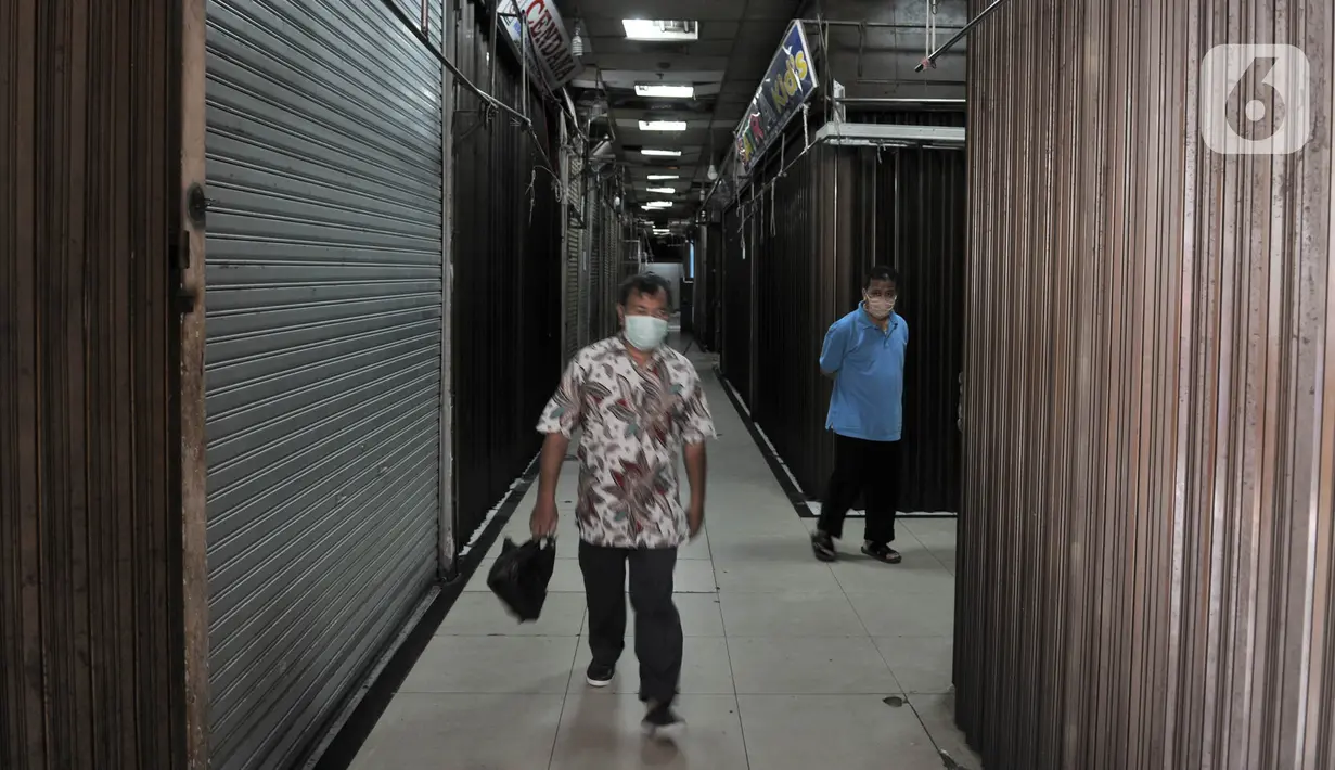 Pengunjung saat melintasi pertokoan yang tutup di Pasar Jatinegara, Jakarta, Kamis (26/3/2020). Pedagang yang masih tetap membuka toko pun mengeluh karena penjualan menurun hingga 80 persen. (merdeka.com/Iqbal S. Nugroho)