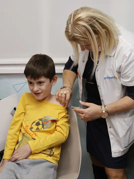 Bocah Israel, Yoav (9) menerima dosis vaksin Covid-19 Pfizer/BioNTech Covid-19 di Meuhedet Healthcare Services Organization di Tel Aviv, saat Israel memulai kampanye vaksinasi virus corona untuk anak berusia 5 hingga 11 tahun, Senin (22/11/2021). (JACK GUEZ / AFP)
