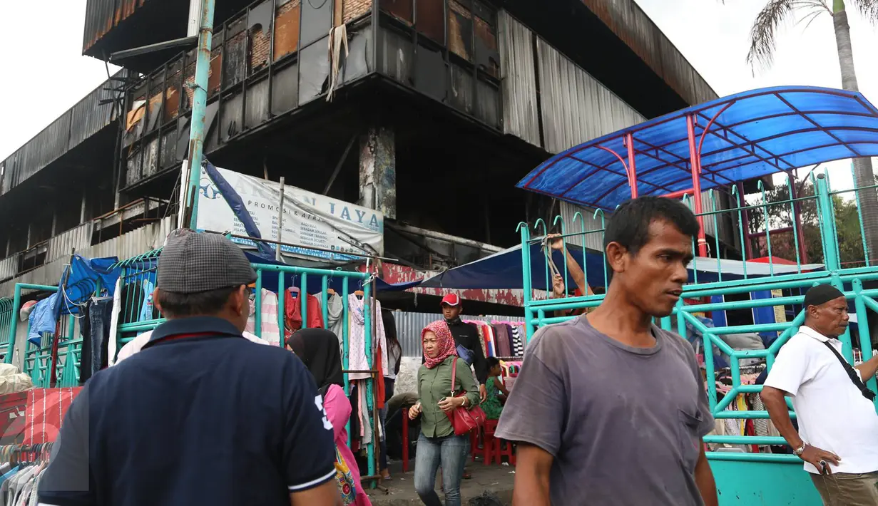 Pengunjung melewati pedagang korban kebakaran yang berjualan di area parkir Pasar Senen, Jakarta, Rabu (8/2). Belum tersedianya tempat penampungan sementara membuat para pedagang terpaksa mendirikan tenda lapak. (Liputan6.com/Immanuel Antonius)