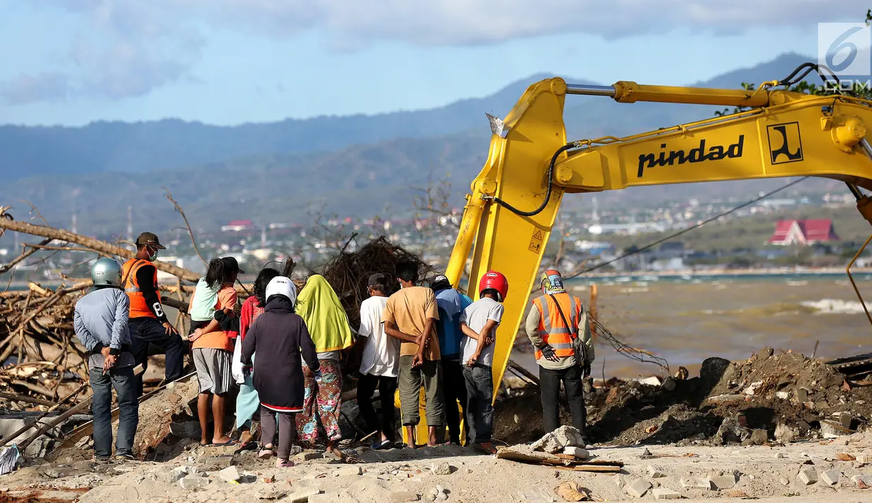 Warga menyaksikan proses evakuasi Nanang Kosim (20) menggunakan alat berat, yang diduga masih tertimbun di dalam tanah pascagempa dan tsunami Palu di Pantai Talise, Sulawesi Tengah, Senin (8/10). (Liputan6.com/Fery Pradolo)
