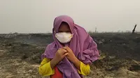Seorang anak mengenakan masker saat bermain di lokasi lahan perusahaan bekas kebakaran hutan di wilayah Kumpeh, Muaro Jambi. Foto diambil tahun 2019. (Liputan6.com / Gresi Plasmanto)