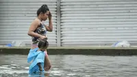 Seorang wanita dan seorang anak mengarungi jalan yang terendam banjir di kota Valenzuela, Filipina pada Rabu, 2 Agustus 2023. (AP Photo/Aaron Favila)
