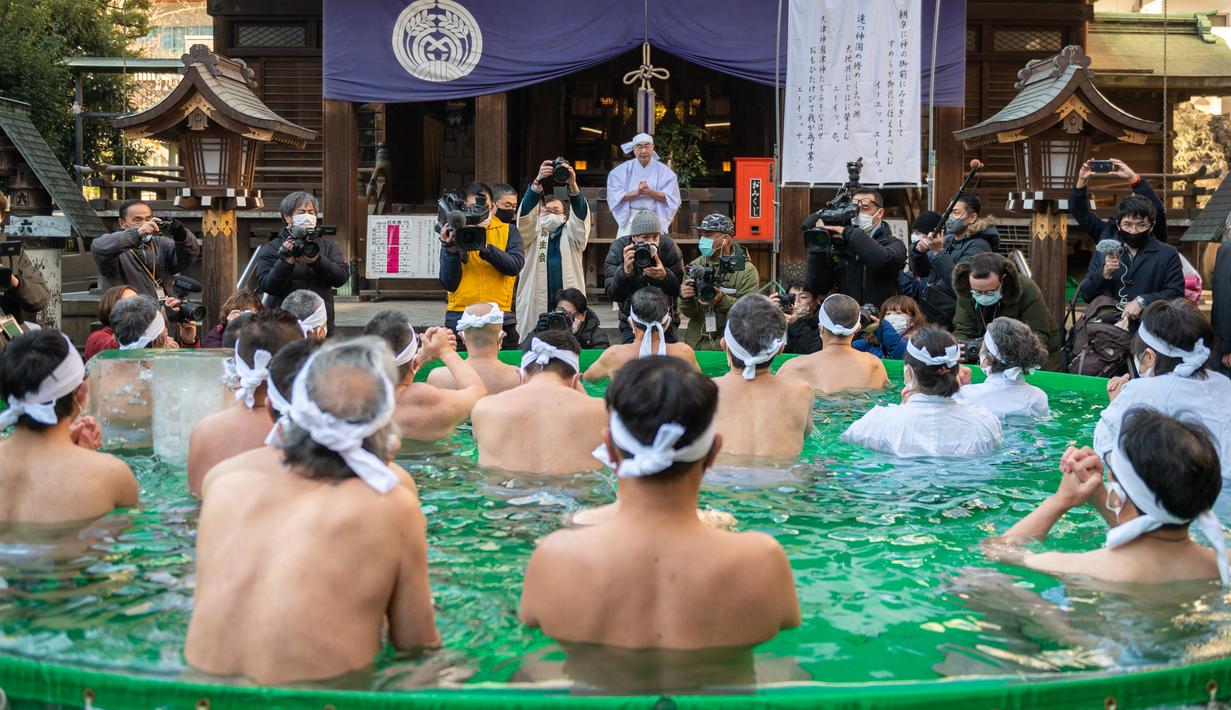 Penganut Shinto dari Kuil Teppozu Inari mandi dengan air dingin untuk mensucikan jiwa dan tubuh mereka selama ritual Tahun Baru di Tokyo, Jepang, Minggu (9/1/2022). Mereka pun satu per satu memasuki bak yang airnya dingin bahkan ada es batu di dalamnya. (Philip FONG/AFP)