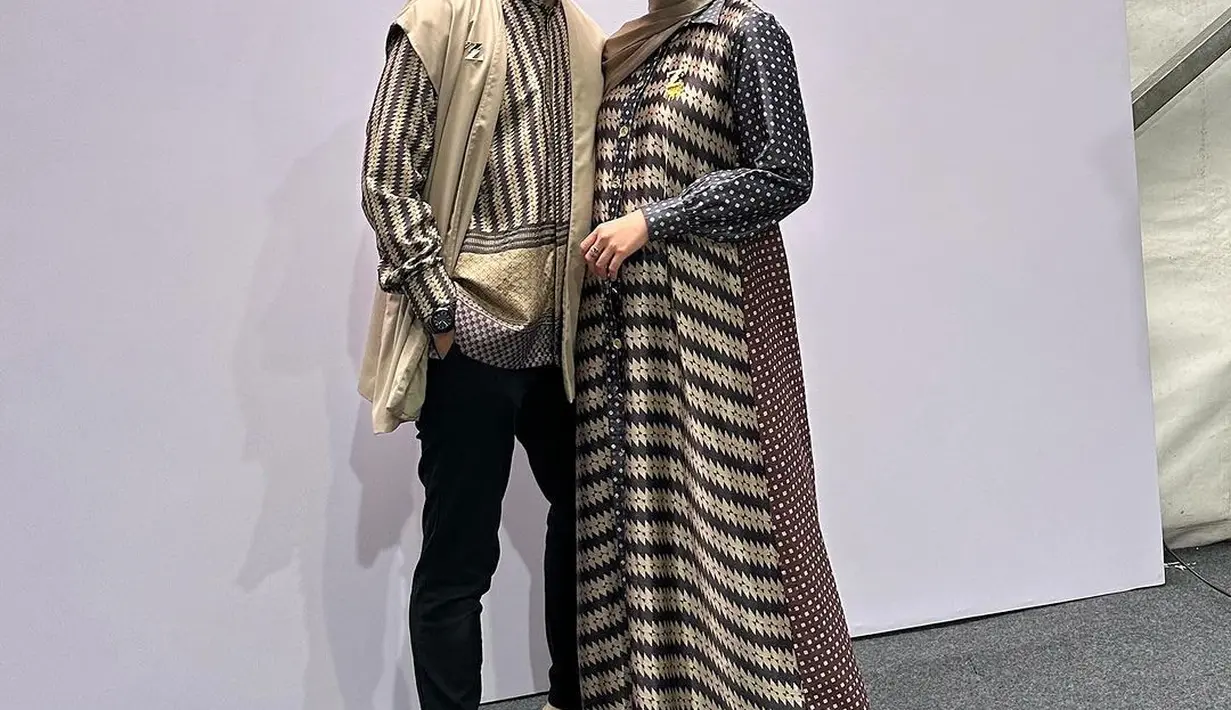 Fenita tampil anggun dengan gamis satin dan hijab gold. Arie Untung terlihat fashionable dengan kemeja lengan panjang dan sleeveles outer polos [@fenitarie]