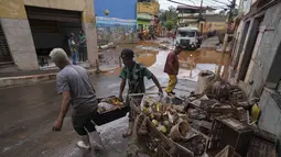 Warga memindahkan barang-barang yang rusak dan makanan busuk setelah banjir di Raposos, negara bagian Minas Gerais, Brasil (11/1/2022). Tanah longsor akibat hujan deras telah menewaskan sedikitnya 12 orang dan pihak berwenang sedang memantau bendungan yang bisa jebol. (AP Photo/Eugenio Savio)