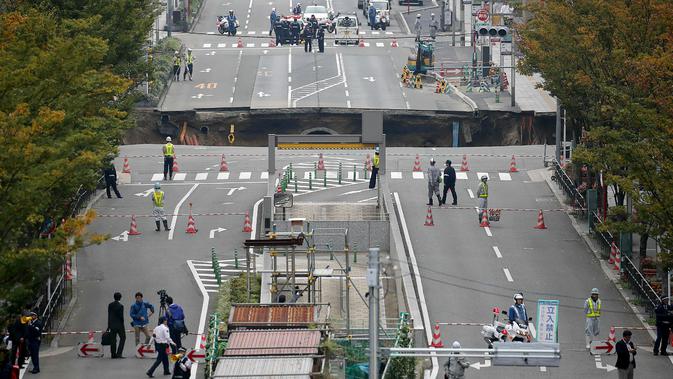 Sejumlah petugas mengamankan lokasi munculnya sebuah lubang raksasa atau yang biasa disebut sinkhole di persimpangan dekat Stasiun Hakata, Fukuoka, Jepang, Selasa (8/11). Jalanan itu tiba-tiba runtuh hingga menciptakan lubang besar. (STR/JIJI PRESS/AFP)