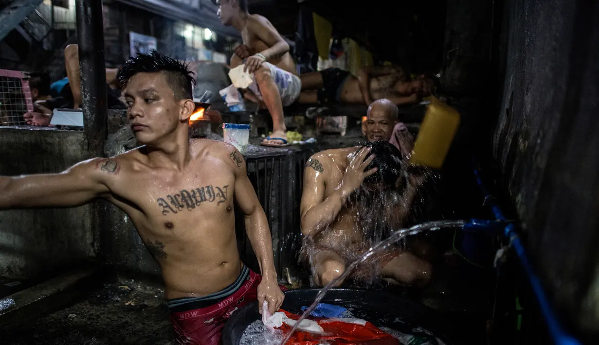 Narapidana memasak makan malam sementara kawannya mandi di dalam penjara Quezon City di Manila, Filipina, 21 Juli 2016. Kondisi sanitasi penjara Quenzon City sangat buruk, hanya terdapat satu toilet yang digunakan hingga 130 narapidana. (Noel Celis/AFP)