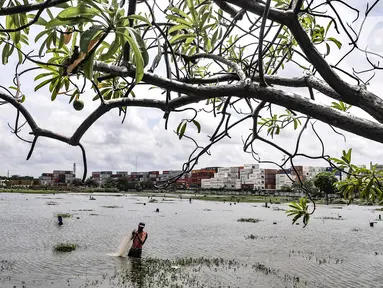 Amir (38) saat menjala ikan di genangan air yang merendam kompleks pemakaman TPU Semper, Jakarta, Selasa (2/2/2021). Banjir yang semakin tinggi merendam TPU Semper hingga mencapai sepinggang orang dewasa. (merdeka.com/Iqbal S. Nugroho)