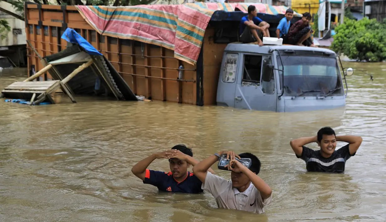 Warga menyeberangi truk yang terendam banjir saat banjir di Lhoksukon, Aceh Utara, Aceh, 3 Januari 2022. Badan Penanggulangan Bencana Daerah (BPBD) Aceh Utara mencatat banjir telah merendam 14 kecamatan di daerah tersebut. (AZWAR IPANK/AFP)