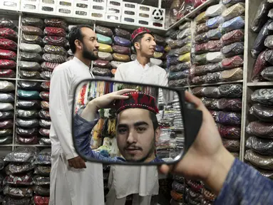 Seorang pria mencoba topi tradisional dalam persiapan untuk bulan puasa Ramadhan yang akan datang, di Peshawar, Pakistan, Sabtu (2/4/2022). Bulan Ramadhan atau sering kita sebut bulan puasa adalah bulan yang di tunggu-tunggu oleh umat Islam di seluruh dunia. (AP Photo/Muhammad Sajjad)