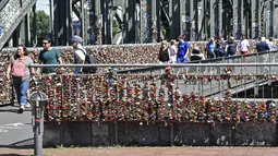 Warga melewati gembok cinta di sebuah jembatan di Cologne, Jerman, Rabu, (5/8/2020). Sebagai bukti cinta mereka, puluhan ribu pasangan telah memasang gembok selama bertahun-tahun ke pagar di Jembatan Hohenzollern sebelum melemparkan kunci ke dalam Sungai Rhein di bawah. (AP Photo/ Martin Meissner)