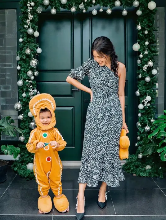 Kali ini, dengan one-shoulder dengan detail mermaid di bagian ujung bawah dress bermotif bunga-bunga kecil dari brand Poise24, Tiffany Soetanto berpose bersama sang buah hati yang mengenakan kostum ginger bread. Foto: Instagram.