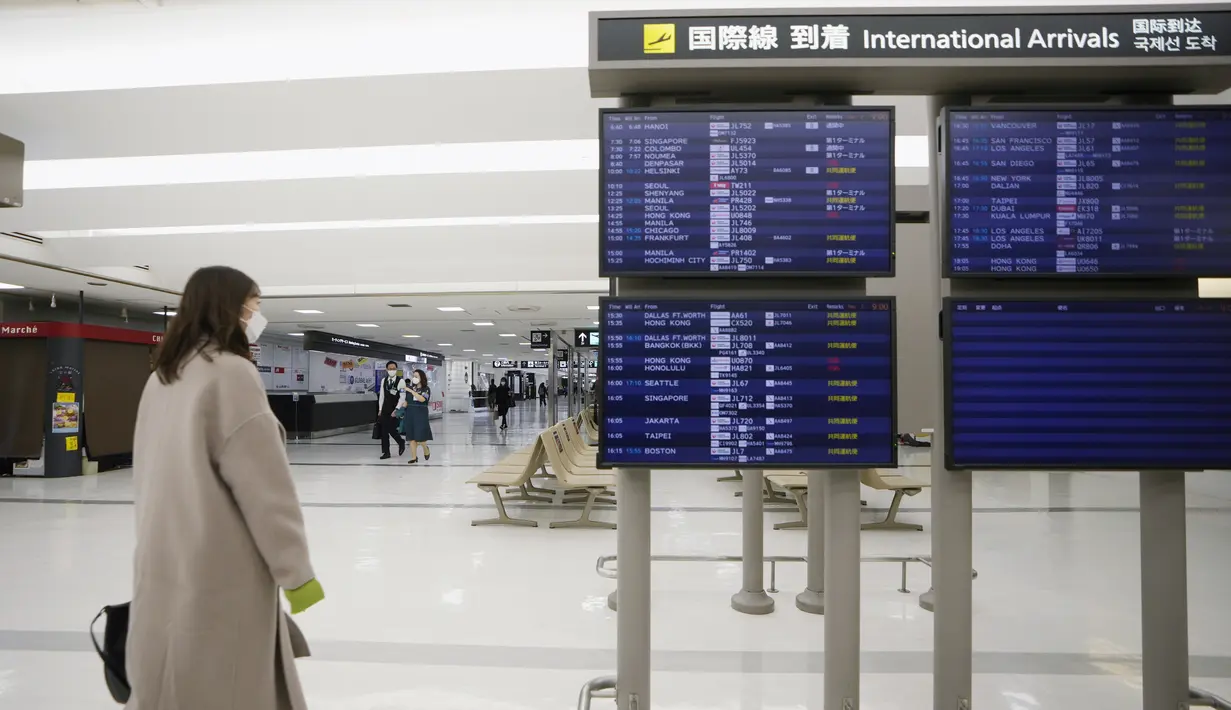 Penumpang berjalan dekat layar jadwal kedatangan penerbangan internasional di Bandara Narita, Tokyo, Kamis (2/12/2021). Maskapai-maskapai internasional diminta menangguhkan reservasi baru pada semua penerbangan masuk ke Jepang hingga akhir Desember terkait varian Omicron. (AP Photo/Hiro Komae)