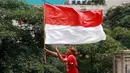 Seorang masyarakat membawa bendera Merah Putih saat menyambut Timnas Indonesia U-22 dan kontingen Indonesia untuk SEA Games 2023 saat pawai Kira87uara yang berlangsung dari Kemenpora hingga GBK, Jakarta, Jumat (19/05/2023). (Bola.com/M Iqbal Ichsan)