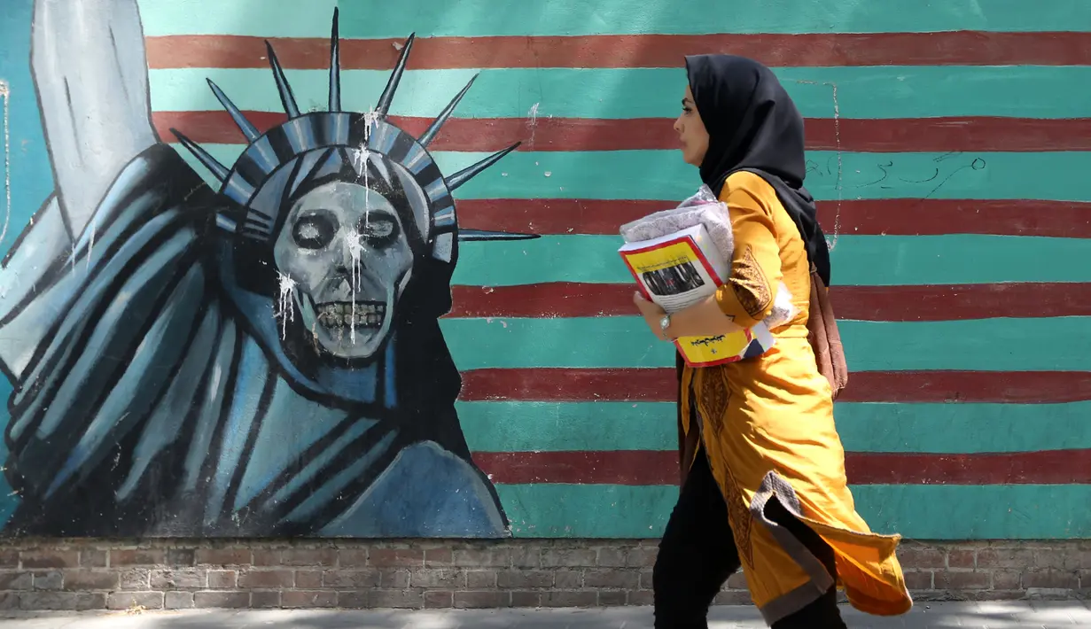 Seorang wanita berjalan melewati lukisan mural yang menggambarkan Patung Liberty di sepanjang dinding bekas Kedutaan Amerika Serikat (AS) di Ibu Kota Teheran, Iran, Sabtu (22/6/2019). (ATTA KENARE/AFP)