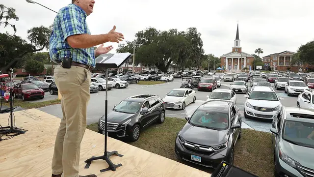 Pastor Cliff Lea berkhotbah di tempat parkir yang penuh dengan mobil selama pelayanan drive-in di Gereja First Baptist Leesburg.