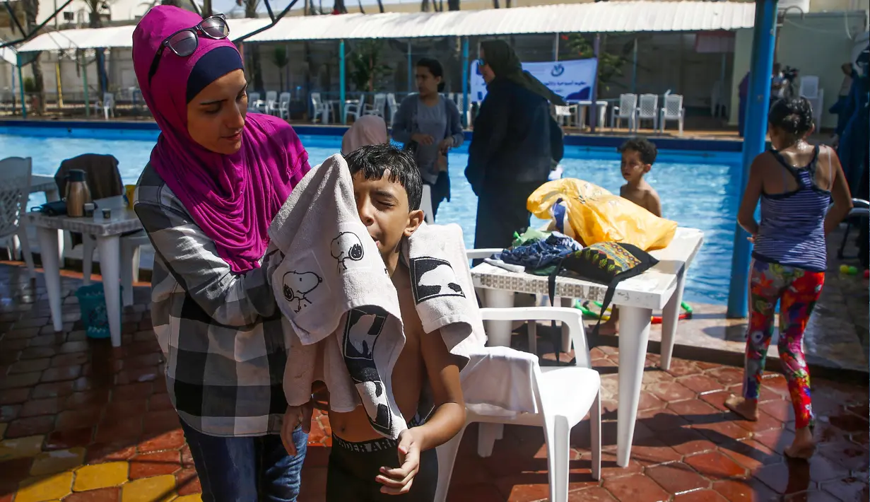 Seorang ibu menyeka wajah anak laki-lakinya yang menderita autisme setelah berpartisipasi dalam sesi terapi renang di Beit Lahia di Jalur Gaza utara, Palestina  (5/8/2019). (AFP Photo/Mohammed Abed)