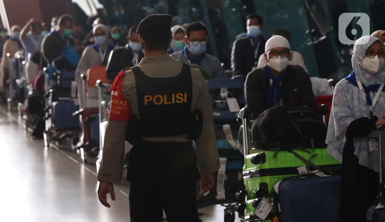 Aparat kepolisian mengamati rombongan jemaah umrah saat tiba di Bandara Soekarno Hatta, Tangerang, Selasa (29/12/2020). Rombongan jemaah umrah yang baru tiba di Indonesia tersebut diarahkan untuk melakukan karantina di tempat yang telah disediakan oleh pemerintah. (Liputan6.com/Angga Yuniar)