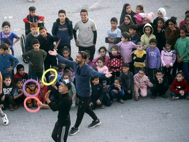 Warga Palestina menampilkan pertunjukan hiburan untuk anak-anak pengungsi yang berlindung di sekolah PBB di kamp pengungsi Rafah, Jalur Gaza selatan, Kamis (23/11/2023). Pertunjukan sederhana cukup membuat anak-anak untuk melupakan sejenak kepedihan mereka di tengah perang Israel dan Hamas di Jalur Gaza. (AP Photo/Mohammed Dahman)