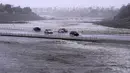 Kendaraan melintasi cekungan pengendali banjir yang hampir mencapai jalan di Palm Desert, California, Minggu, 20 Agustus 2023.(AP Photo/Mark J. Terrill)