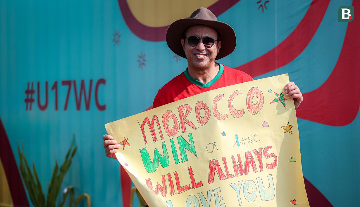 <p>Suporter Maroko, Mohammad Aziz Mrabat berpose dengan membentangkan poster bertuliskan "Maroko, menang atau kalah aku tetap mencintaimu" menjelang laga kedua Grup A Piala Dunia U-17 2023 antara Timnas Maroko U-17 melawan Timnas Ekuador U-17 di Stadion Gelora Bung Tomo (GBT), Surabaya, Senin (14/11/2023). (Bola.com/Bagaskara Lazuardi)</p>