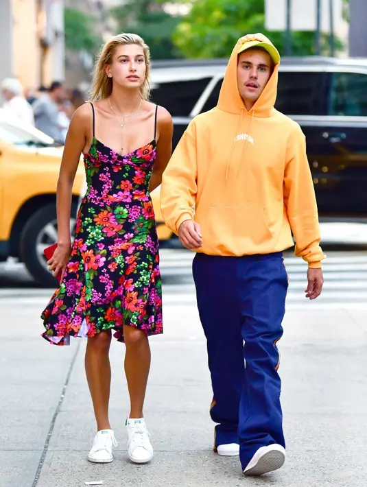 Kalau yang ini, Hailey Baldwin nampak cantik dengan dress bunga-bunga yang menggambarkan musim panas. Sementara Justin memakai hoodie orange dan celana biru. (James Devaney/GC Images/USWeekly)