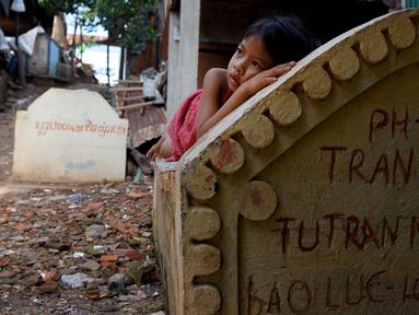 Seorang anak perempuan berbaring di atas sebuah kuburan di Phnom Penh, Kamboja pada 5 Juni 2019. Pemakaman menjadi tempat peristirahatan abadi bagi orang mati, tetapi area pemakaman ini menjelma sebagai tempat tinggal untuk bertahan hidup bagi mereka yang didera kemiskinan. (TANG CHHIN Sothy/AFP)