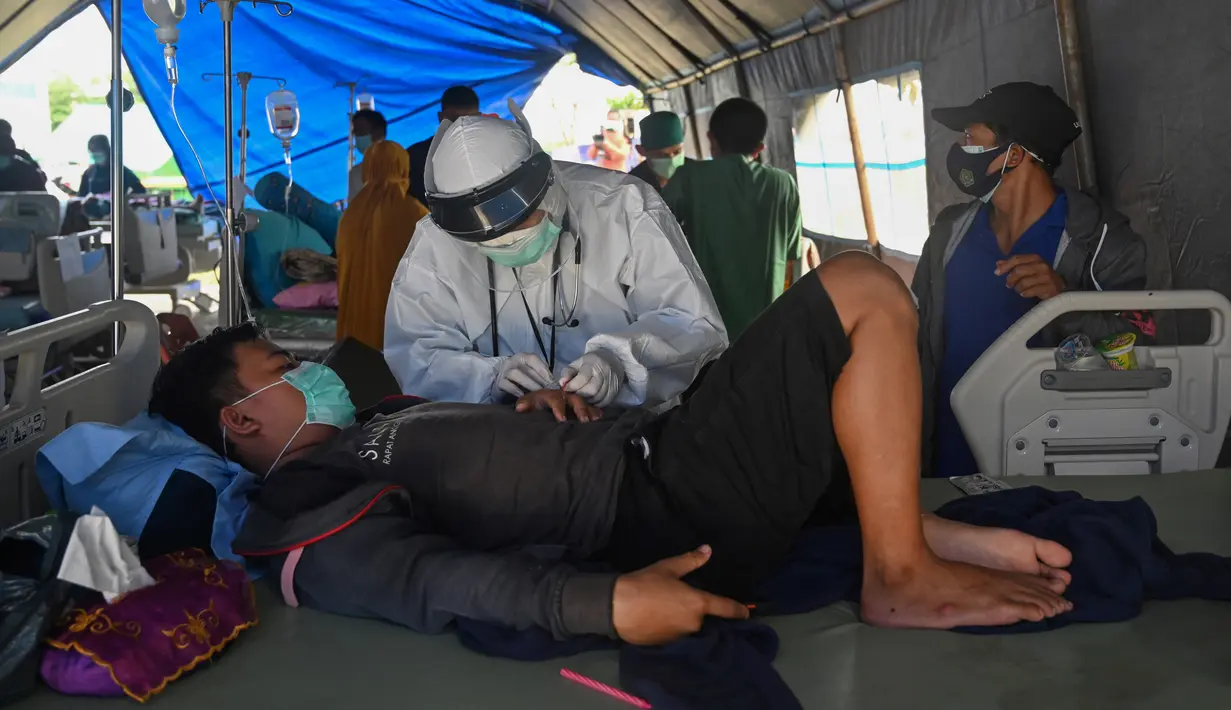 Seorang pria yang terluka dalam gempa dengan magnitudo 6,2 menerima perawatan di tempat penampungan sementara di luar Rumah Sakit Regional Sulbar, Mamuju, Sulawesi Barat, Minggu (17/1/2021). Mereka dirawat di dalam tenda darurat untuk mengantisipasi gempa susulan. (ADEK BERRY/AFP)
