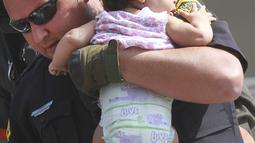 Seorang polisi Hazleton menggendong seorang bayi setelah kebakaran terjadi di sebuah gedung apartemen di Hazleton, Pennsylvania (26/7/2019). Pemadam kebakaran kota menggunakan truk menyelamatkan penghuni dari lantai tiga gedung. (Warren Ruda/Hazleton Standard-Speaker via AP)