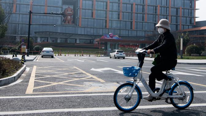 Seorang wanita bermasker mengendarai sepeda di depan kantor pusat Alibaba di Kota Hangzhou, Provinsi Zhejiang, China, Rabu (5/2/2020). Pemerintah Hangzhou memberlakukan pembatasan pergerakan bagi warganya menyusul mewabahnya virus corona. (NOEL CELIS/AFP)