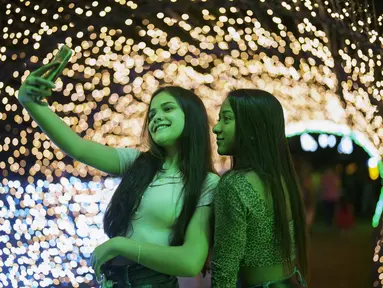 Dua wanita berfoto selfie di acara lampu Natal di taman Ibirapuera di Sao Paulo, Brasil, Selasa (14/12/2021). Jelang perayaan Natal, taman dan pantai dihiasi lampu-lampu yang indah. (AP Photo/Andre Penner)