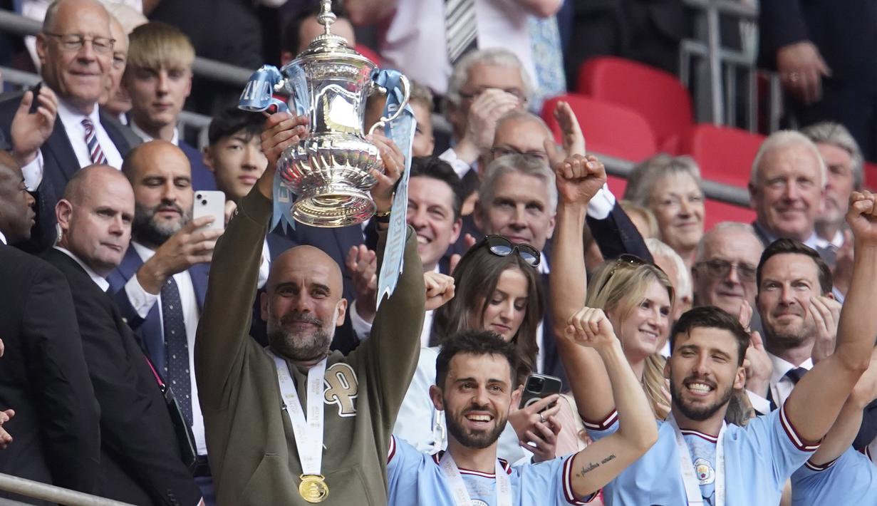 Pelatih Manchester City, Pep Guardiola (kiri) mengangkat trofi Piala FA setelah berhasil membawa Manchester City keluar sebagai juara dalam pertandingan final FA Cup 2022/2023 melawan Manchester United yang berlangsung di Wembley, Sabtu (3/6/2023) WIB. (AP Photo/Dave Thompson)