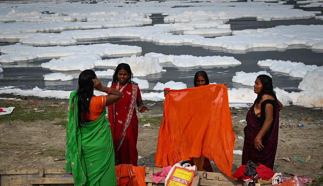 Sejumlah wanita membersihkan diri seusai mandi di sungai Yamuna sebagai bagian dari ritual untuk festival Chhath Puja yang akan datang di New Delhi, Senin (8/11/2021). Sungai yang sangat dianggap suci oleh umat Hindu India ini dipenuhi lapisan busa karena limbah beracun. (Sajjad HUSSAIN / AFP)