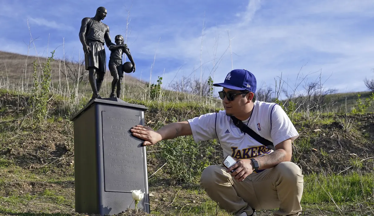 Oscar Romero menyentuh patung untuk mengenang Kobe Bryant dan putrinya, Gianna di Calabasas, California, Rabu (26/1/2022). Patung tersebut dibawa seniman Dan Medina, di jalan setapak dekat lokasi Bryant, putrinya dan tujuh orang lainnya tewas dalam kecelakaan helikopter pada 2020. (AP/Ashley Landis)