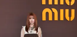 Momo TWICE tampil dengan gaya playful bernuansa vintage. Ia mengenakan mini dress cokelat bersiluet babydoll yang dipadukan dengan panel rajut krem pada bagian atas. Aksen scarf bermotif warna-warni di leher menambah sentuhan retro yang khas. [Dok/Miu Miu].