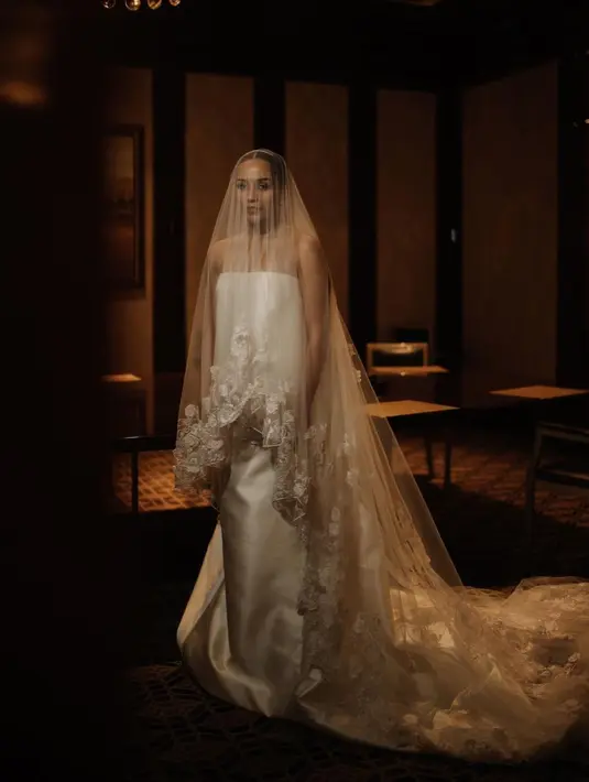 Angel Pieters tampil elegan dengan gaun putih slik off shoulder dari desainer Monica Ivena. Gaun tersebut dipadukan dengan veil yang memiliki detail bordiran bunga warna putih di ujungnya.