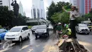 Sejumlah petugas membersihkan batang pohon yang tumbang di jalan Jenderal Sudirman, Jakarta, Senin (1/2). Pohon tumbang yang terjadi saat hujan deras mengakibatkan kemacetan panjang dikawasan tersebut. (Liputan6.com/Helmi Afandi)