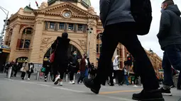 Orang-orang berjalan di luar Stasiun Flinders Street di pusat kota Melbourne ketika pihak berwenang mengumumkan lockdown untuk keenam kalinya di kota itu, pada Kamis (5/8/2021).  Lockdown di kota terpadat kedua di Australia tersebut guna mengendalikan penyebaran Covid varian delta. (Con Chronis/AFP)
