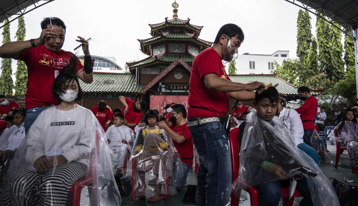 Penata rambut melakukan cukur rambut gratis saat acara amal di Surabaya, Jawa Timur, Senin (8/11/2021). Layanan cukur rambut gratis ini dilakukan kepada 100 anak yatim piatu. (Juni Kriswanto/AFP)