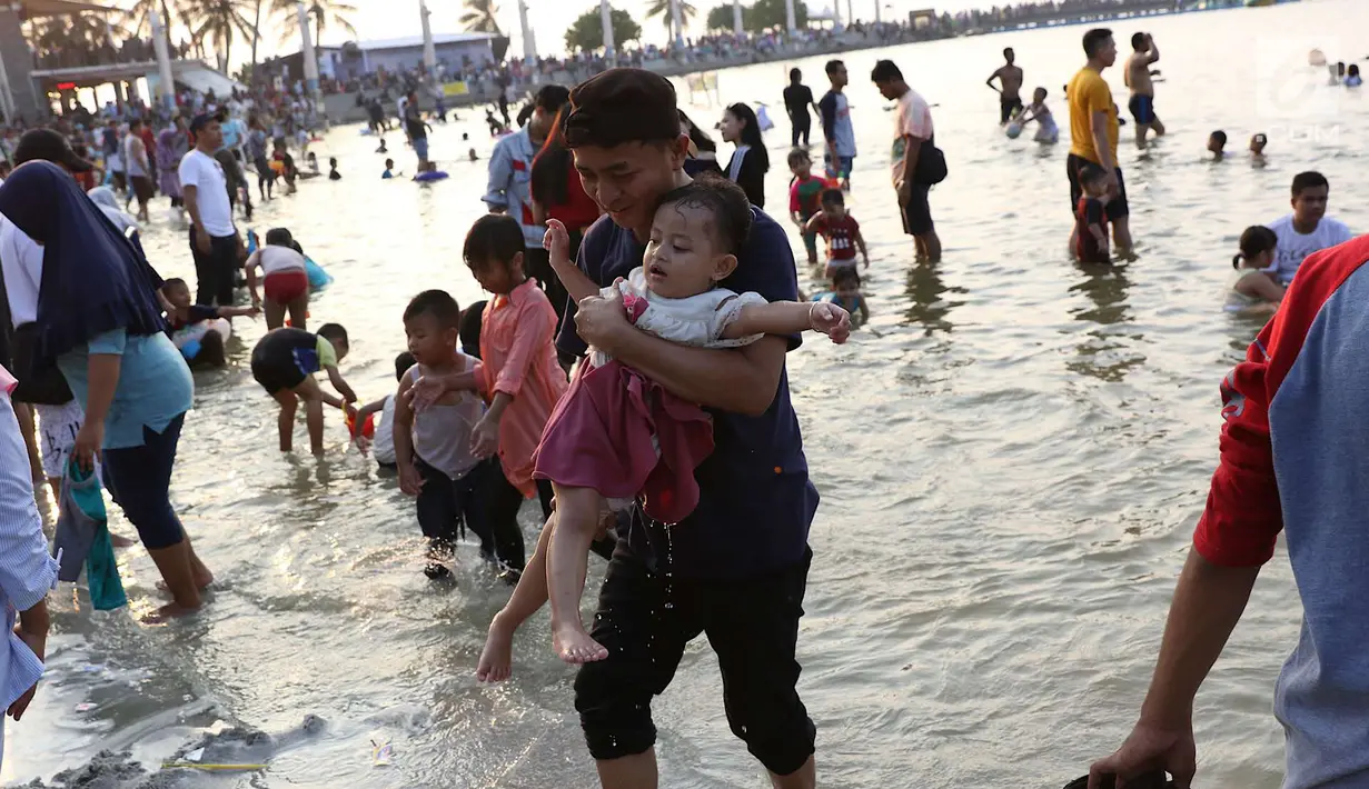 Seorang pengunjung menggendong balita saat berwisata di Pantai Karnaval Ancol, Jakarta, Sabtu (16/6). H+1 libur Lebaran, jumlah pengunjung di Ancol mencapai 88.143 orang. (Liputan6.com/Immanuel Antonius)