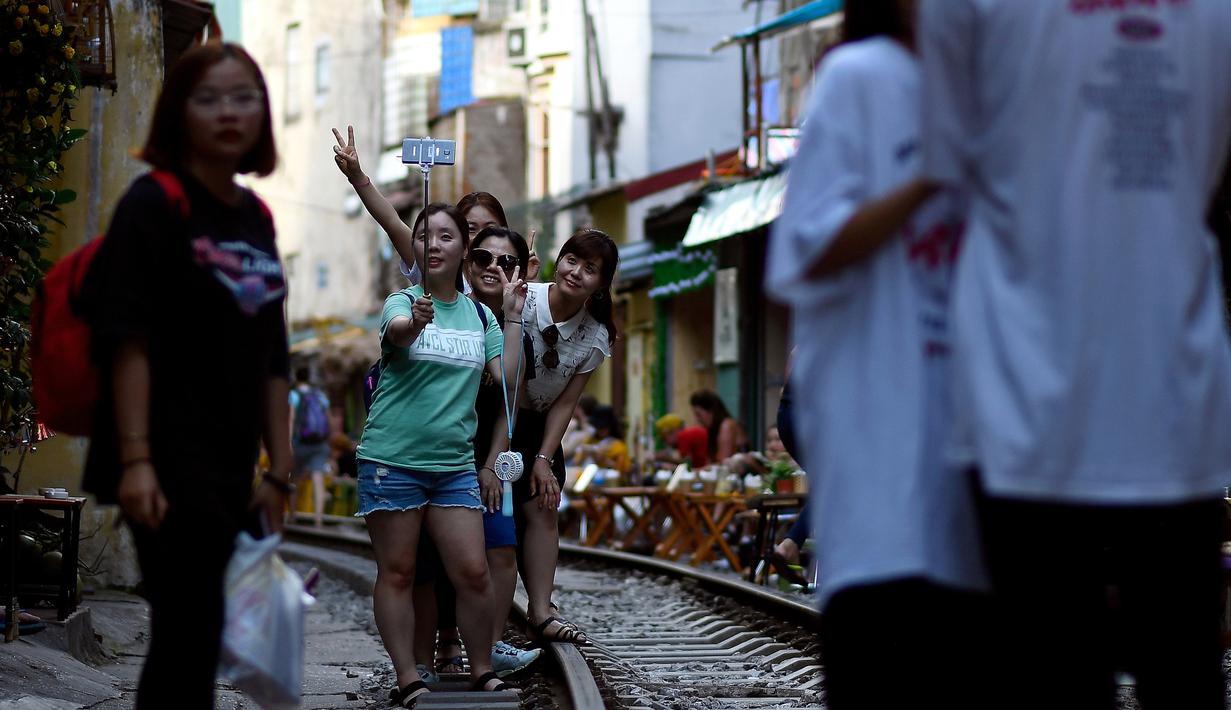 Foto pada 8 Juni 2019 memperlihatkan wisatawan berswafoto di tengah jalur kereta api populer di Hanoi. Turis sengaja datang ke Old Quarter untuk berfoto di rel kereta api yang dianggap ' instagramable' tersebut. (Photo by Manan VATSYAYANA / AFP)
