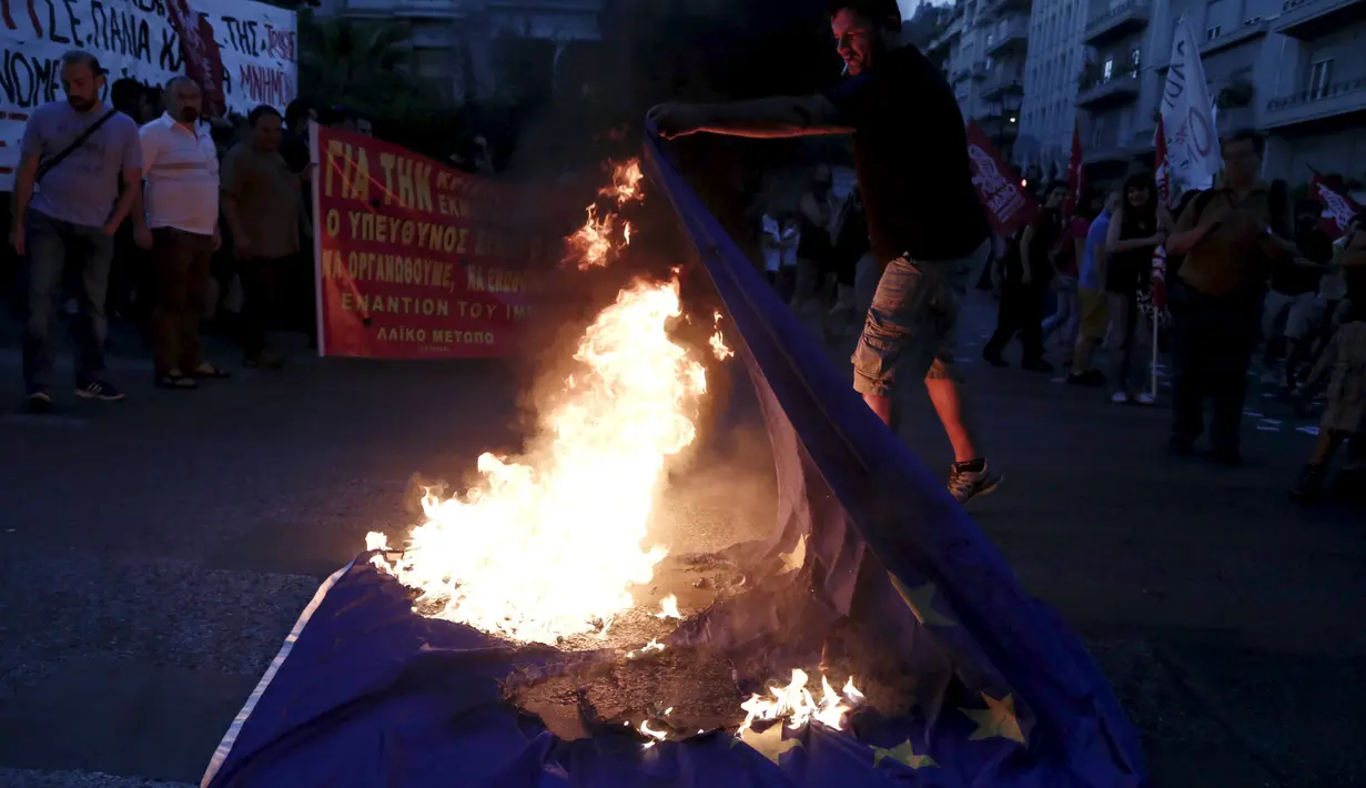 Seorang pengunjuk rasa anti-Euro membakar bendera Uni Eropa di Athena, Yunani, (2/7/2015). PM Alexis Tsipras mengatakan tutupnya bank tidak akan lama setelah adanya kontrak baru dengan kreditur setelah referendum. (REUTERS/Panayiotis Tzamaros)