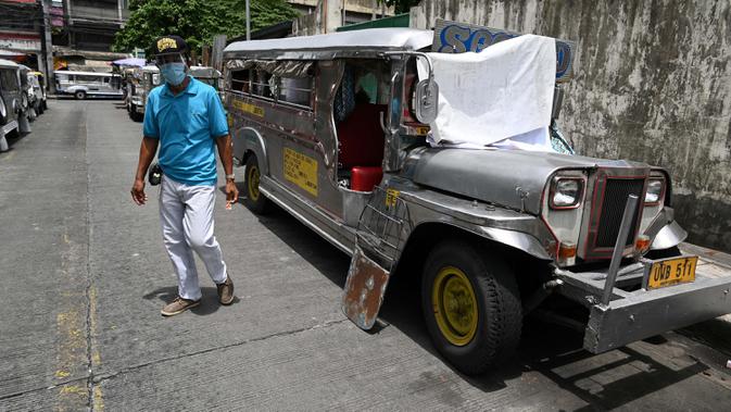 Warga melewati jeepney yang berfungsi sebagai rumah sementara yang diparkir di sepanjang jalan di Manila, 12 Agustus 2020. Angkutan ikonik di Filipina itu belum dapat mengangkut penumpang sejak Maret akibat lockdown Covid-19 yang membuat jutaan orang kehilangan pekerjaan. (Ted ALJIBE/AFP)